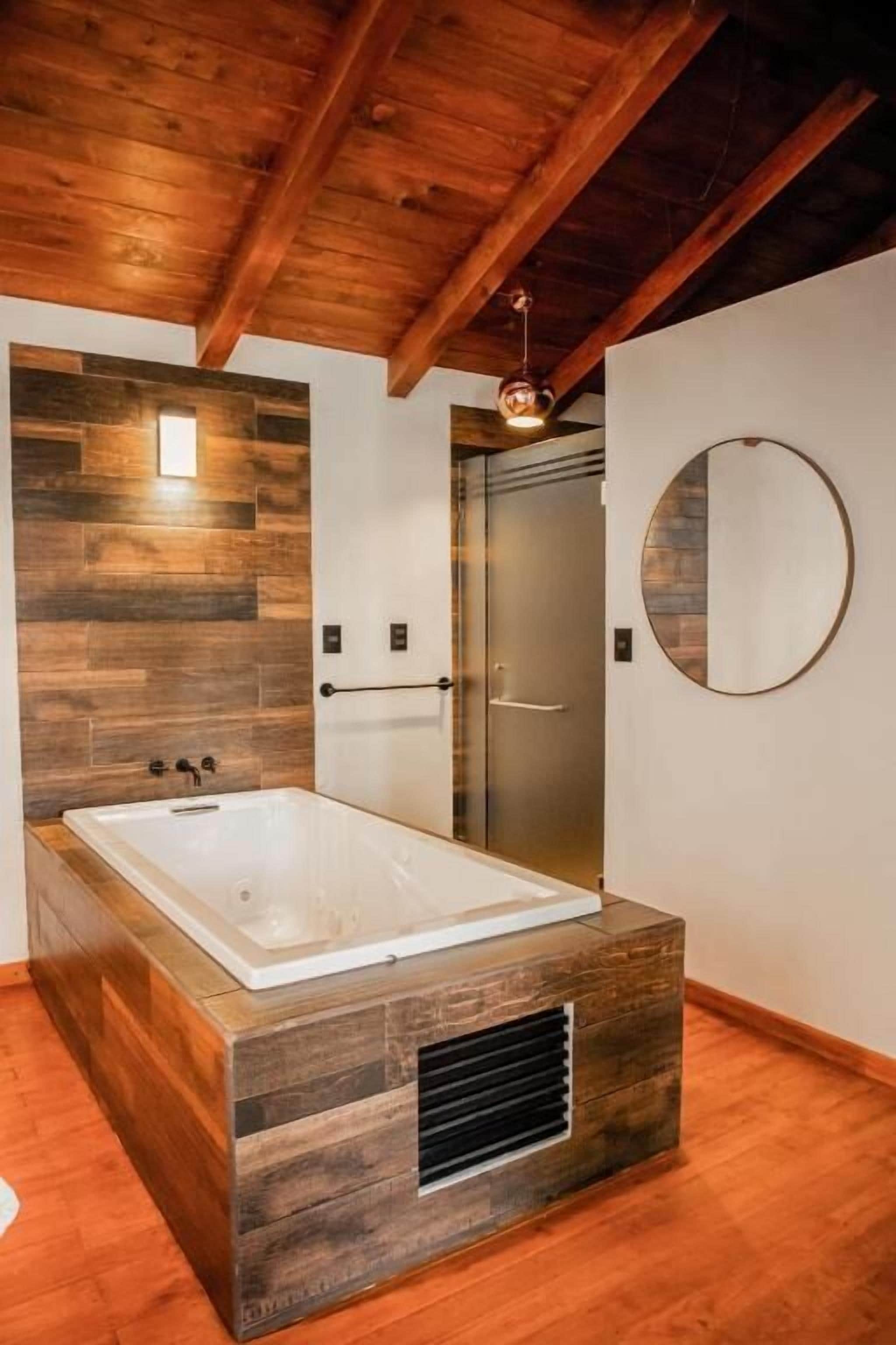 A modern bathroom with a wooden vanity, a freestanding bathtub, and a large mirror on the wall.