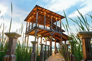 A wooden gazebo with a tiled floor and a metal railing, surrounded by tall grass. - Hotel Boutique La Casa Del Lago (Tzintzuntzan)