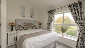 A bedroom with a large bed, a nightstand with a vase of flowers, and a window with curtains. - Manchester House Retreat (Manchester)