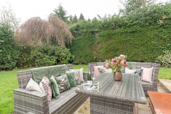 An outdoor seating area with wicker furniture and a table set with a bottle and flowers.
