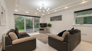 A modern living room with two sofas, a flat-screen TV, a plant, and a large window with a view of greenery. - Manchester House Retreat (Manchester)