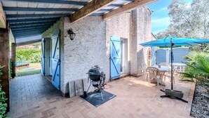 An outdoor patio with a barbecue grill, a table with chairs, and a blue umbrella. - La Pinède, a welcoming family home, 5 minutes from Vallon Pont D'Arc (salavas)