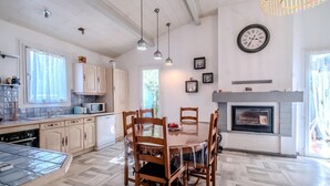 A modern kitchen with wooden cabinets, a dining table with chairs, a microwave, and a fireplace. - La Pinède, a welcoming family home, 5 minutes from Vallon Pont D'Arc (salavas)