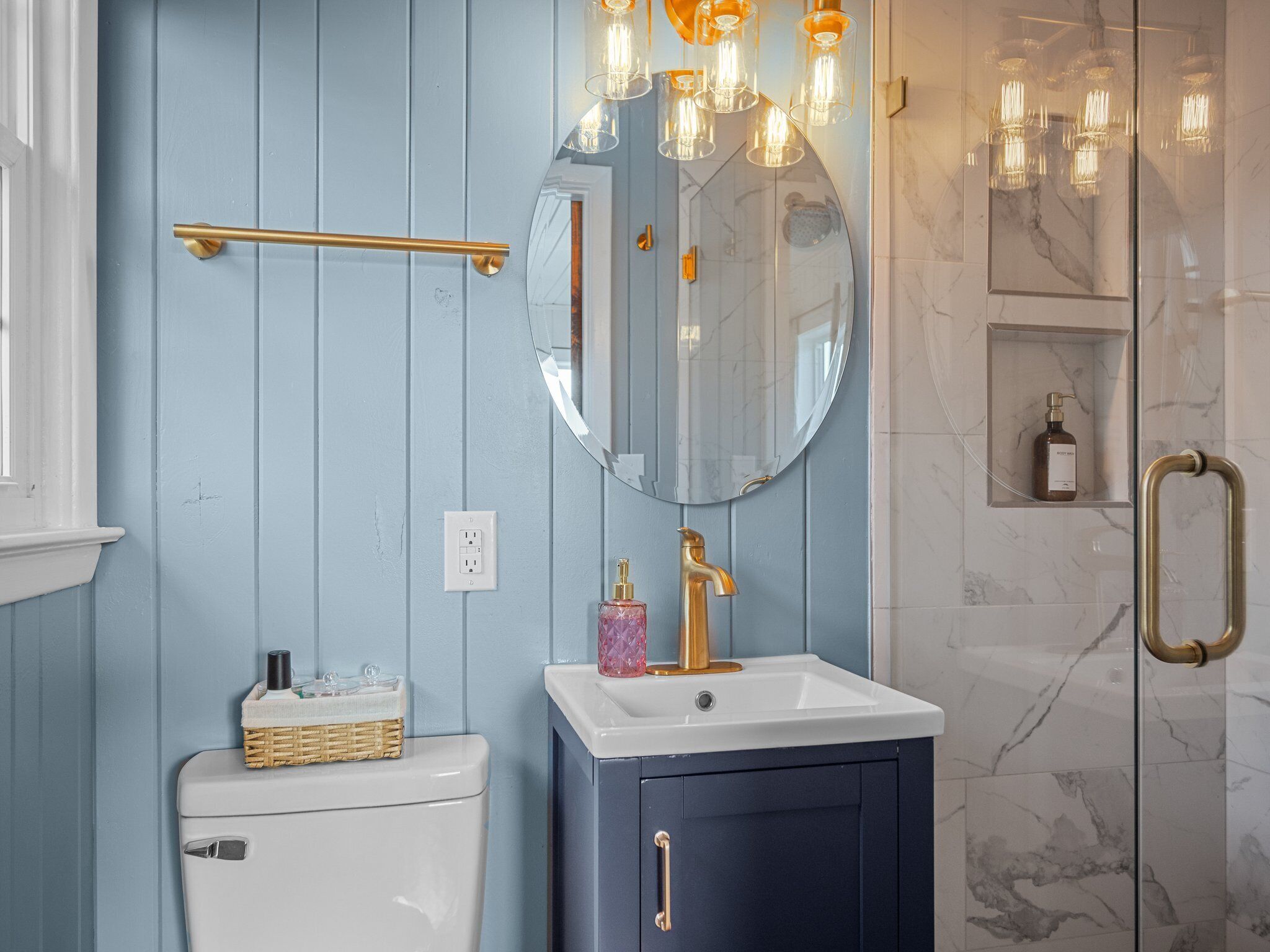 A bathroom with a white toilet, a blue vanity with a gold faucet, a mirror, and a shower with a glass door.