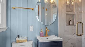 A bathroom with a white toilet, a blue vanity with a gold faucet, a mirror, and a shower with a glass door.