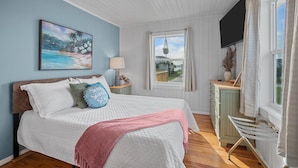 A bedroom with a bed, a painting, a window with curtains, a lamp, and a view of the outside.