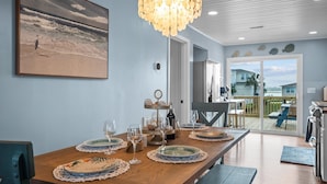 A dining area with a wooden table set for four, a chandelier, and a beach-themed painting on the wall.