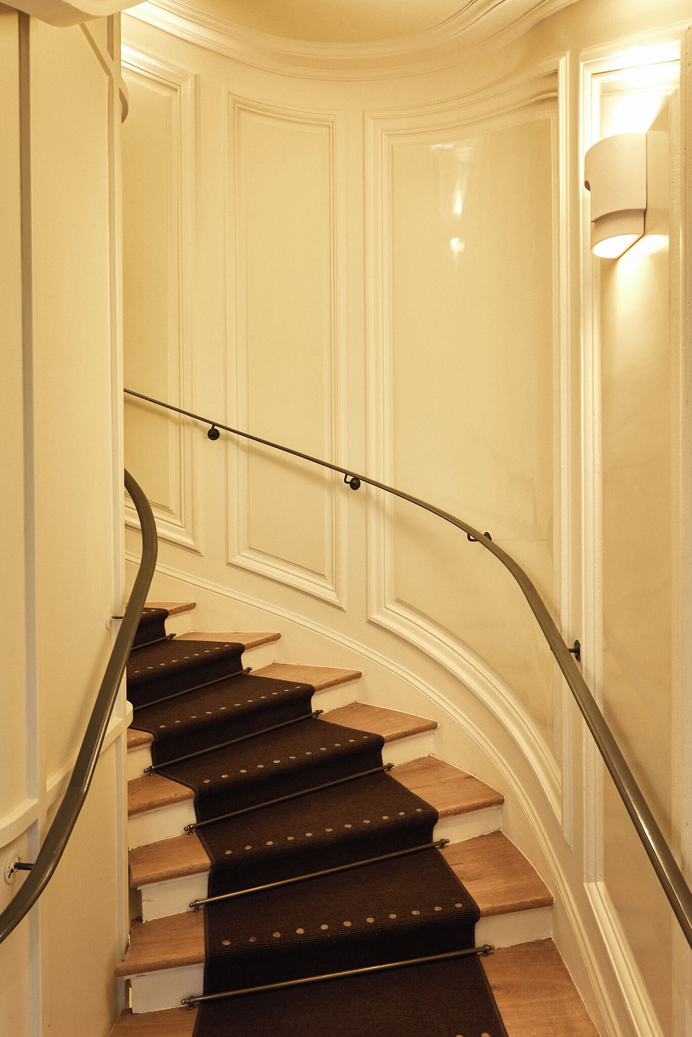 Una scala a forma di curva con corrimano, gradini in legno e un pianerottolo rivestito di moquette.