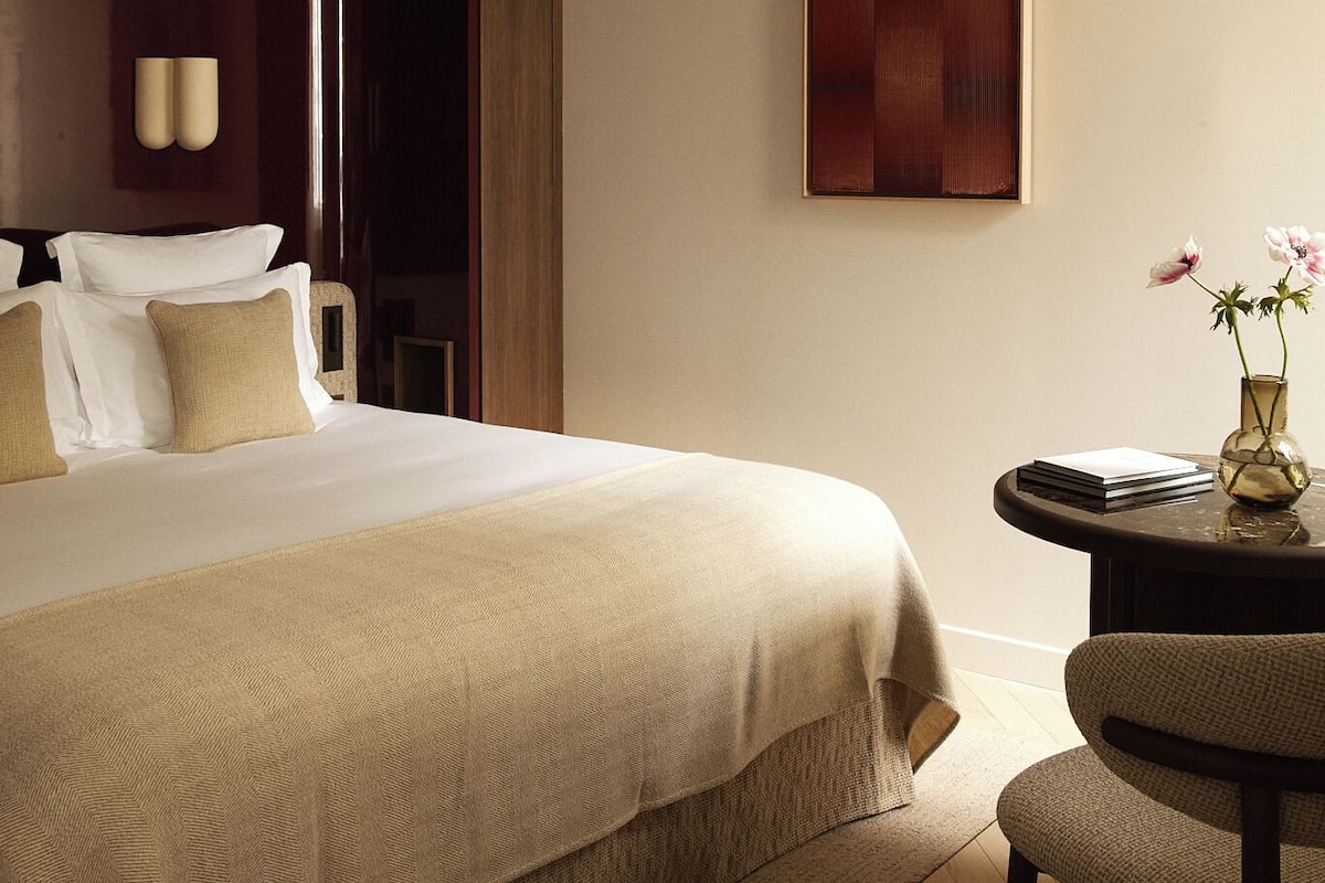 A hotel room with a large bed, a small table with a vase, and a painting on the wall.