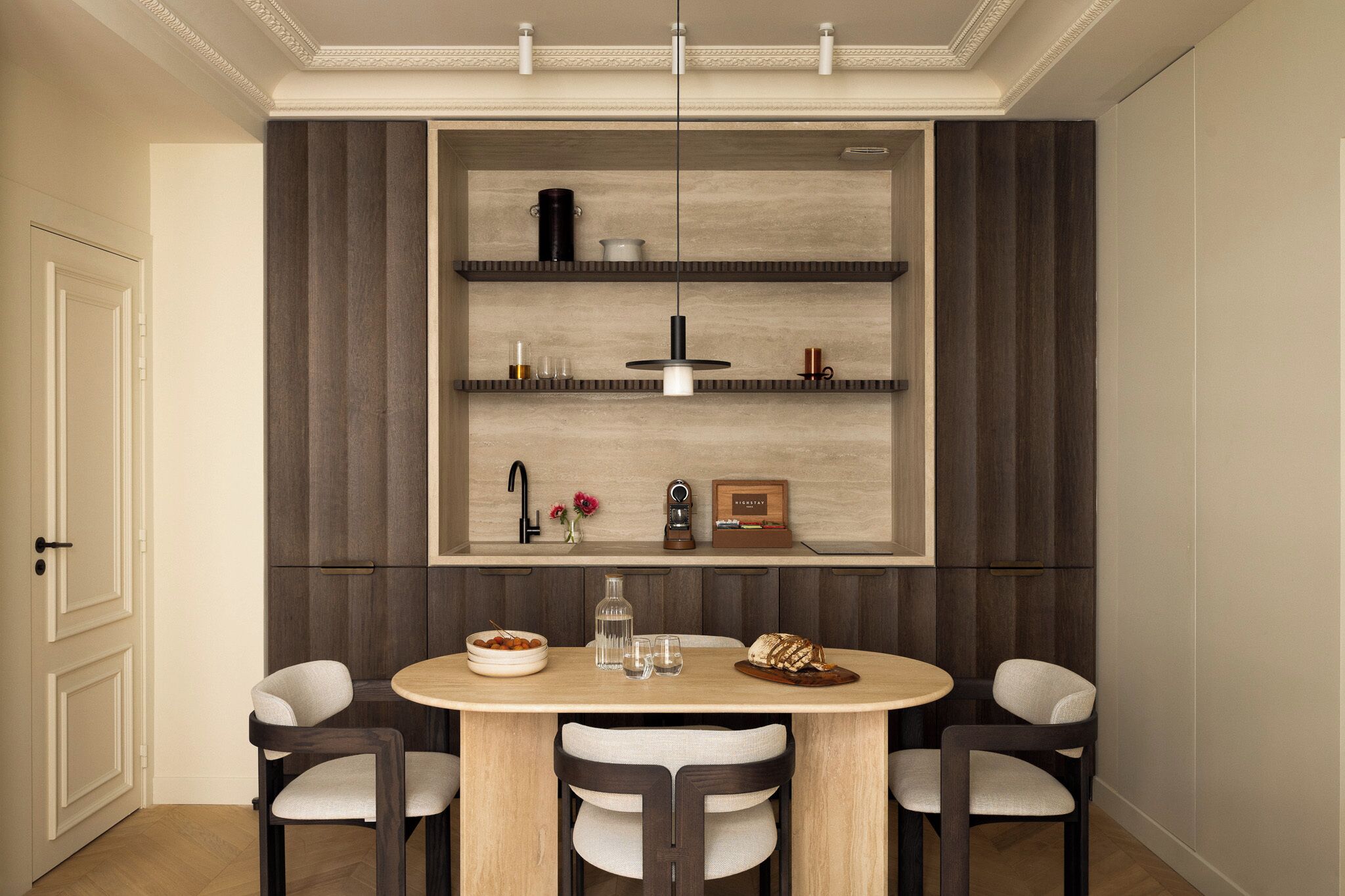 A dining area with a round table, two chairs, a pendant light, and built-in shelves above.