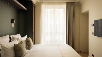 Habitación de hotel con una cama grande, un televisor de pantalla plana y vistas al exterior a través de cortinas translúcidas.