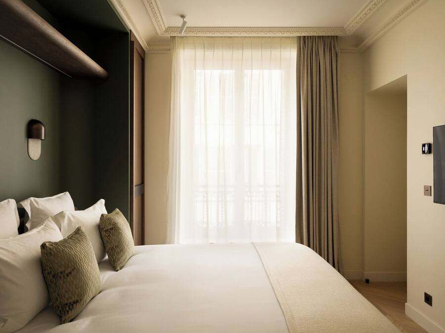 Habitación de hotel con una cama grande, un televisor de pantalla plana y vistas al exterior a través de cortinas translúcidas.