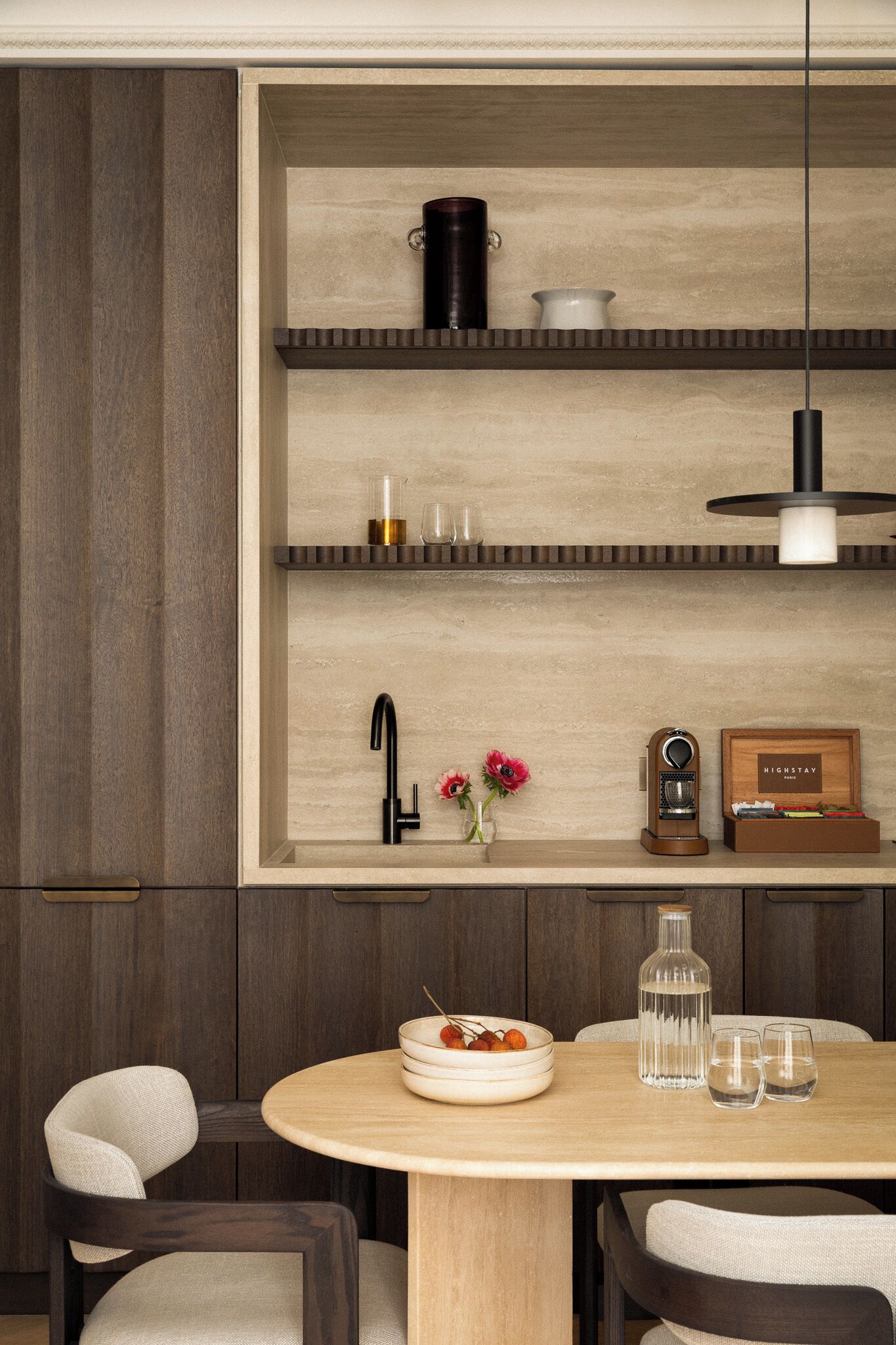 A modern kitchen with wooden cabinets, a round dining table, and a built-in shelf with kitchenware.