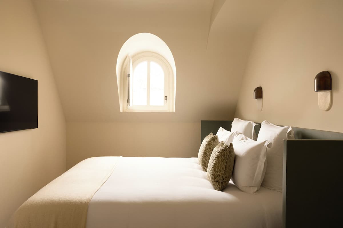 A bedroom with a bed, a window, and a wall-mounted light fixture.