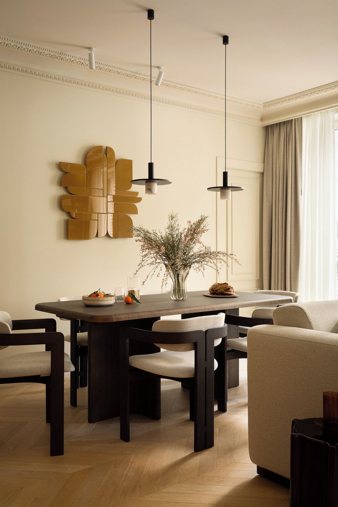 Un espace repas comprenant une table en bois, des chaises, des luminaires suspendus et un élément décoratif mural.
