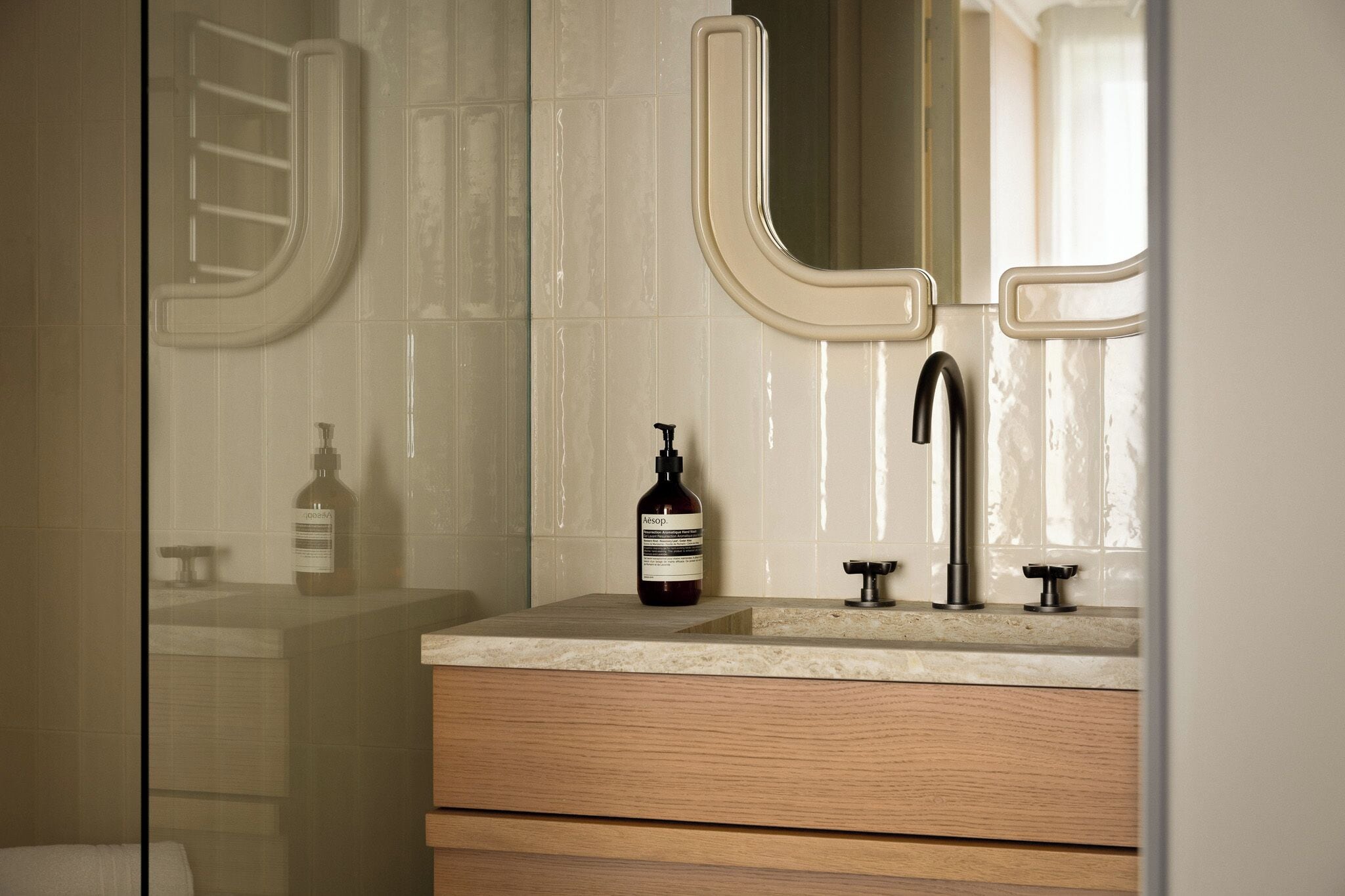 A bathroom with a glass shower enclosure, a wooden vanity with a sink, a mirror, and a bottle of hand soap.