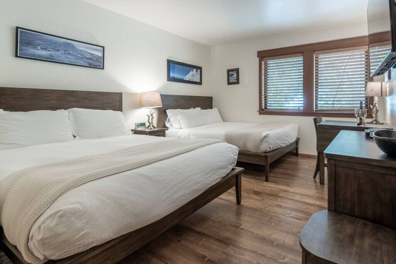 Une chambre d’hôtel avec deux lits, un bureau et une fenêtre avec des stores.