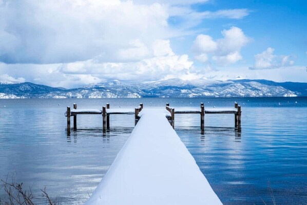 A snow-covered pier extending into a calm body of water with mountains in the background.