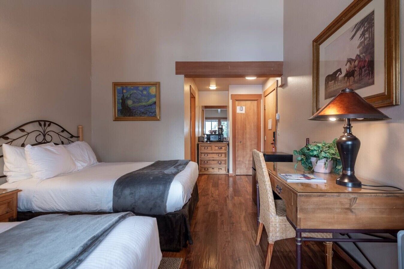 A bedroom with two beds, a desk, a chair, a lamp, and a painting on the wall.