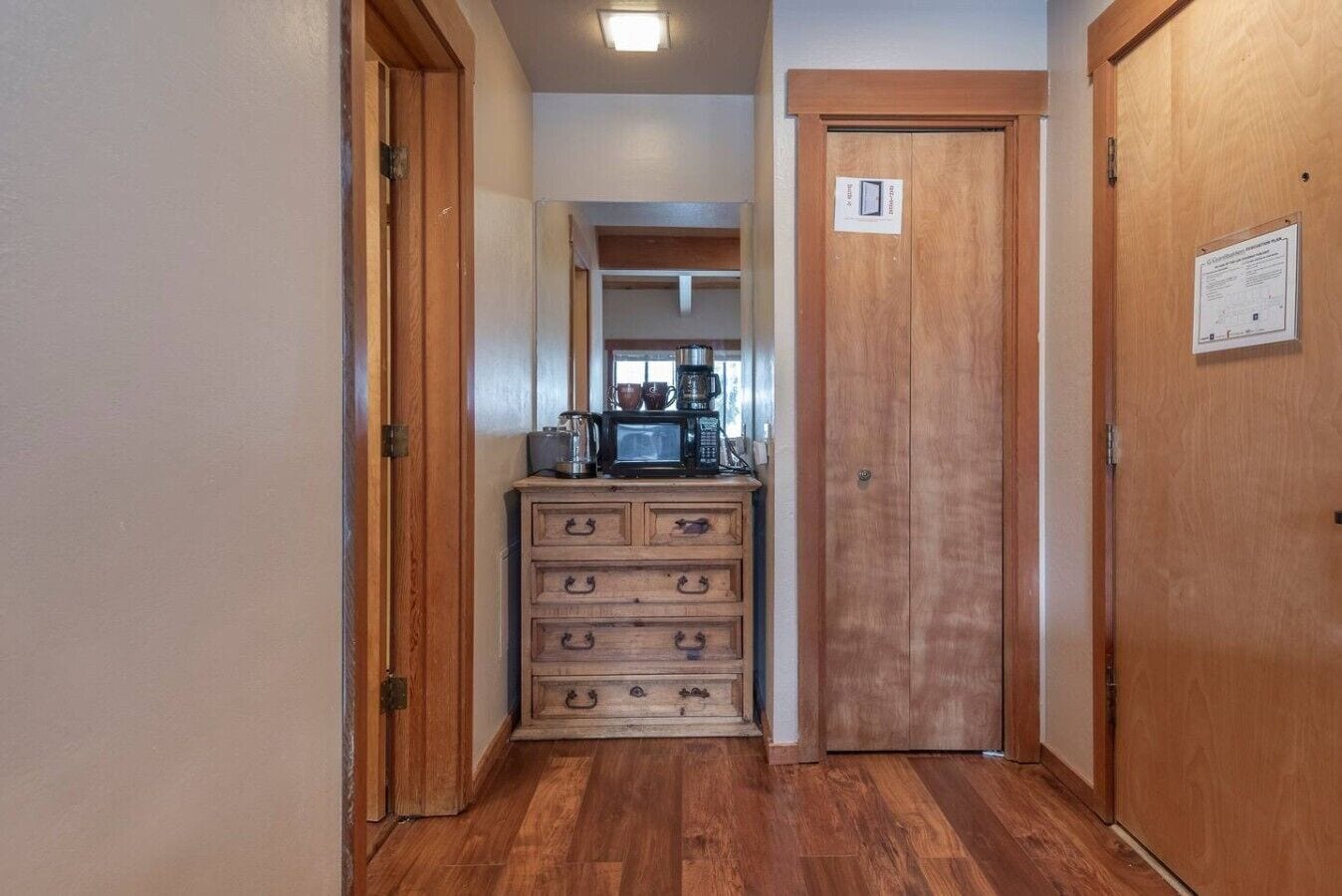A narrow hallway with wooden doors, a wooden dresser with drawers, and a coffee maker on top.