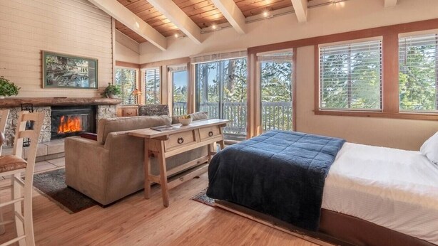 Un dormitorio con chimenea, un sofá, una cama y ventanas amplias.