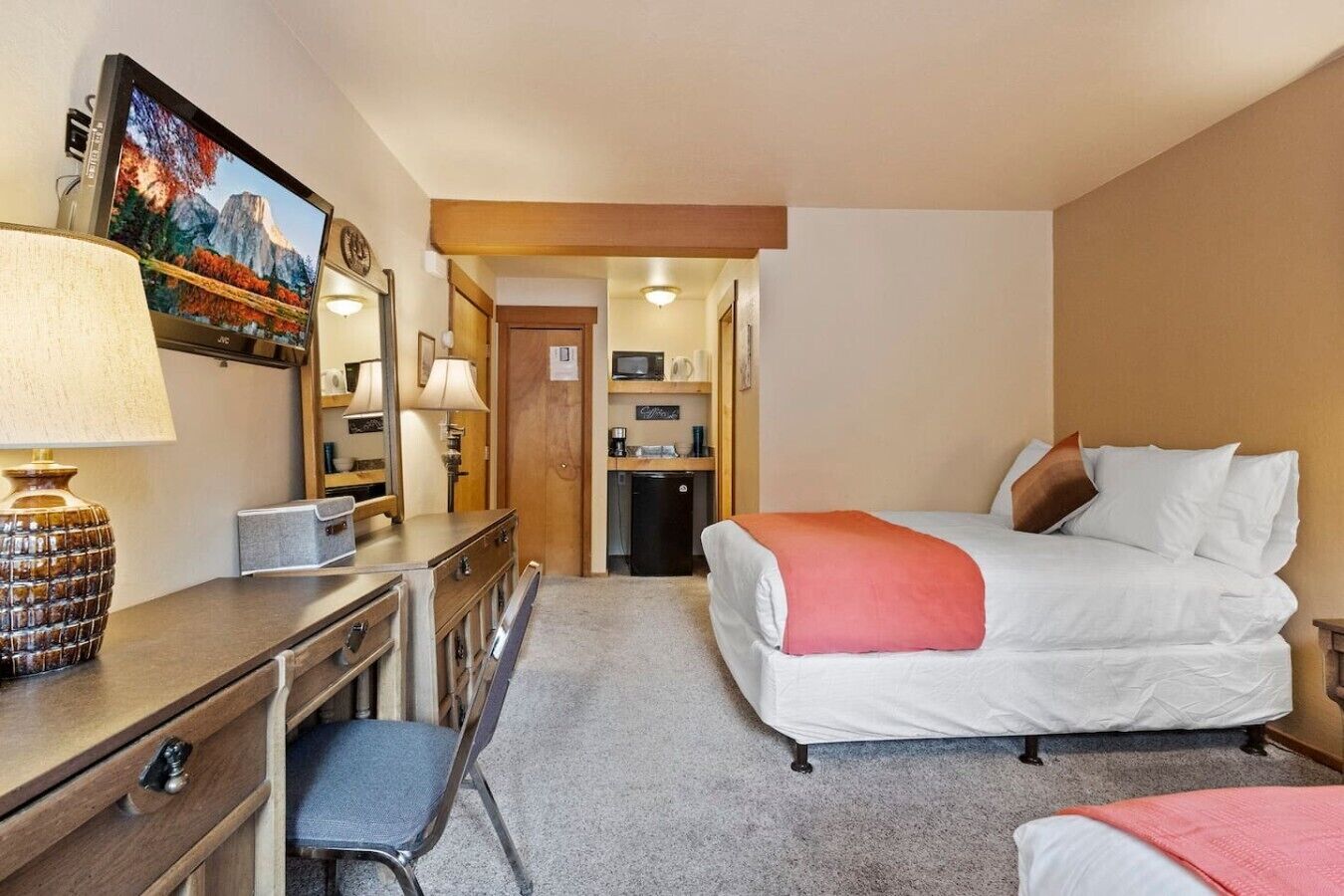Quarto de hotel com cama, escrivaninha, cadeira e televisão exibindo uma paisagem de montanhas.