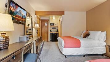 Quarto de hotel com cama, escrivaninha, cadeira e televisão exibindo uma paisagem de montanhas.