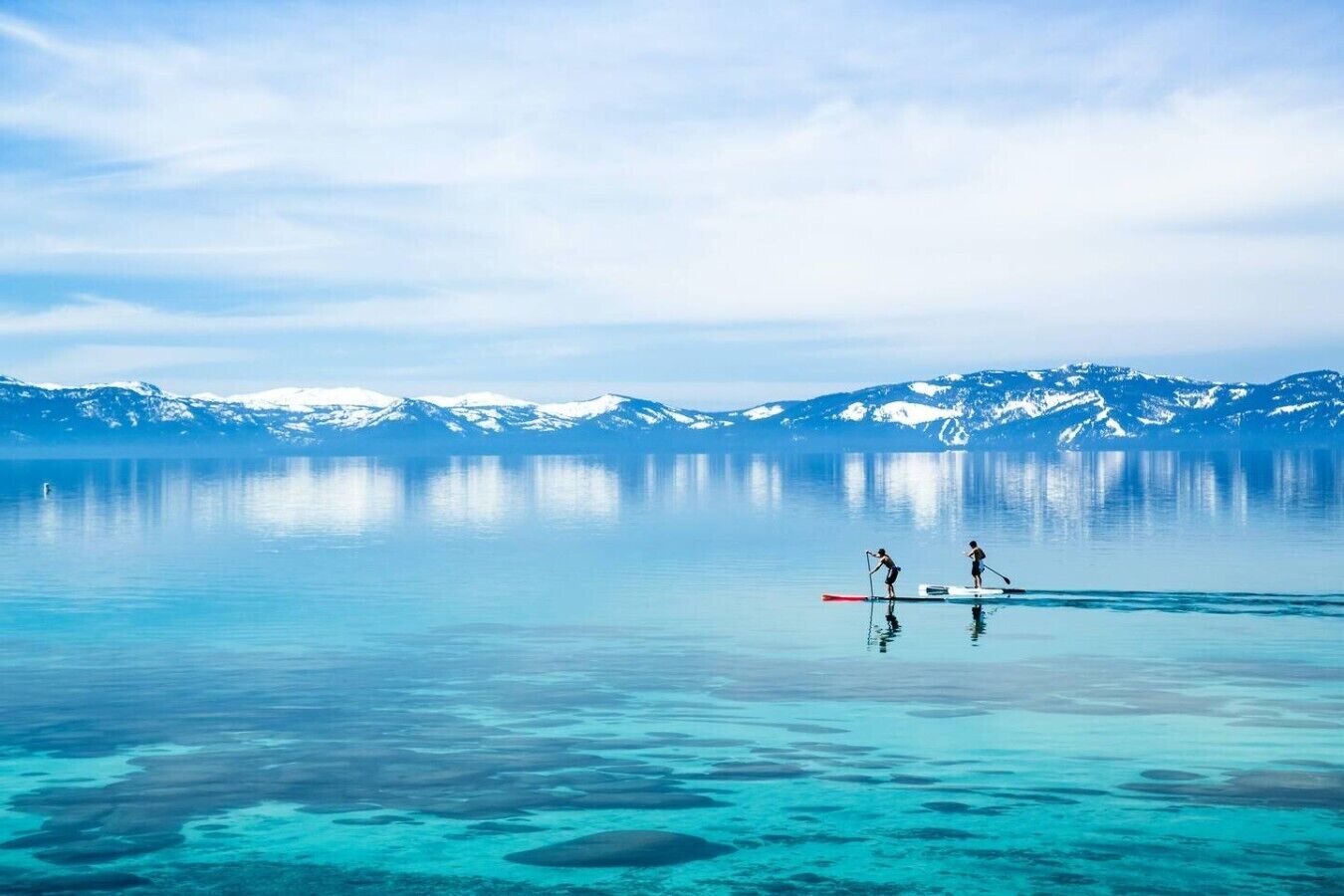 Un lago tranquilo con aguas azules cristalinas y montañas nevadas al fondo.