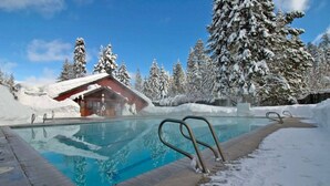 A swimming pool with metal railings, surrounded by snow-covered trees and a building with a red roof.