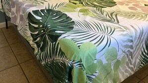 A bed with a tropical leaf-patterned bedspread, a nightstand with a lamp, and a wall with star and heart decorations. - Neverland apartment (Jacksonville)