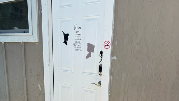 A white door with stickers, a doormat, and a small garden area with plants and a pair of shoes. - Neverland apartment (Jacksonville)