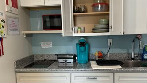 A kitchen with white cabinets, a microwave, a coffee maker, and a sink. - Neverland apartment (Jacksonville)