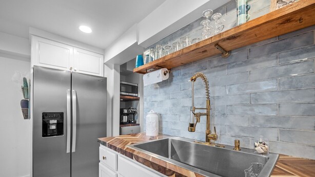 A modern kitchen with a stainless steel refrigerator, a wooden countertop, a built-in sink, and a backsplash with blue tiles. - Cozy beach studio- Bottom unit (Holly Ridge)