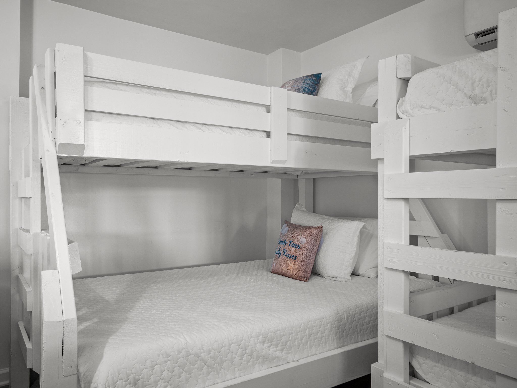 A bunk bed room with white bedding and a pillow with text.