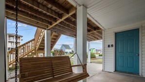 A wooden bench under a covered porch with a blue door and a staircase leading to an upper level. - Cozy beach studio- Bottom unit (Holly Ridge)