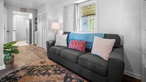 A living room with a grey sofa, a patterned rug, and a window with blinds. - Cozy beach studio- Bottom unit (Holly Ridge)