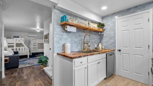 A modern kitchen with white cabinetry, a marble countertop, and a built-in sink. There is a wooden shelf above the sink with decorative items. - Cozy beach studio- Bottom unit (Holly Ridge)