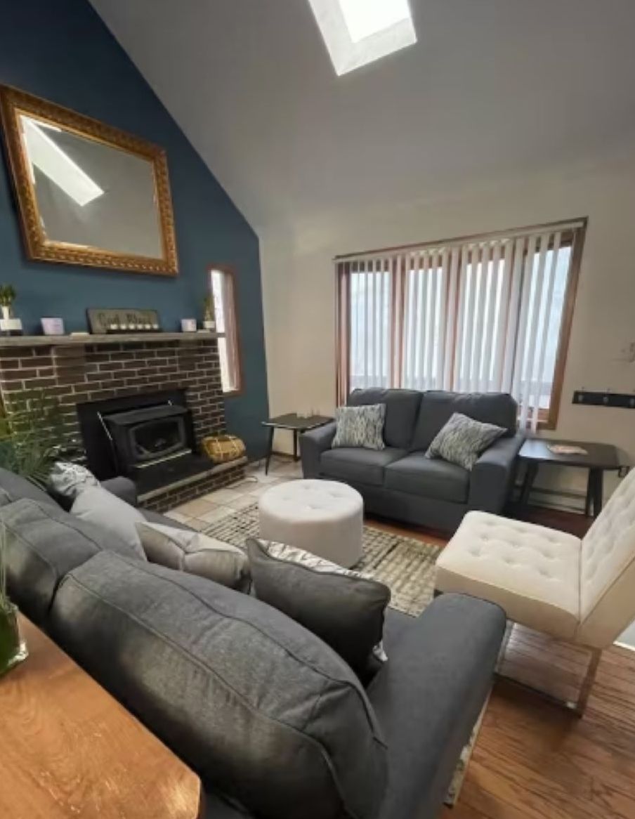 A living room with a fireplace, a sofa set, a coffee table, and a large window with blinds.