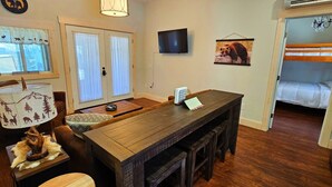 Una cocina compacta con una mesa de madera, un televisor montado en la pared y un adorno en la pared con temática de osos.