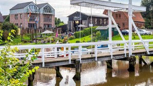 Vista al río con un muelle de madera, un edificio de ladrillo y un restaurante con terraza.