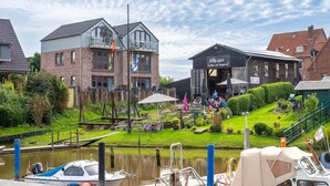 Un entorno junto al río con un restaurante ribereño, un edificio de madera y un muelle con barcos.