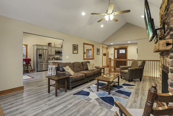 A spacious living room with a high ceiling, a fireplace, and a kitchen in the background.