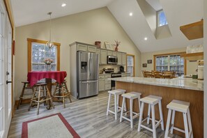 A modern kitchen with a large island, bar stools, and a dining area with a red tablecloth.