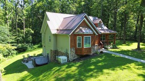 A two-story log cabin with a metal roof, surrounded by a well-maintained lawn and dense forest. - The Wildrose | Hocking Hills, Hot Tub, Karaoke (Logan)