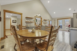 A dining area with a round wooden table and chairs, a kitchen in the background, and a large mirror above the table.
