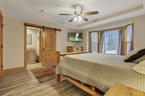 A bedroom with a bed, wooden wardrobe, TV, and large windows.