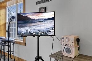 Ein Zimmer mit einem großen Fernseher auf einem Stativ, einem Vintage-Mikrofon und einem Barhocker.