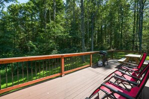 A deck with a wooden railing, a grill, and red lounge chairs.