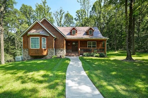 A log cabin with a stone foundation, a metal roof, and a front porch.