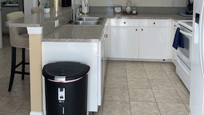 A kitchen with white cabinets, a granite countertop, a ceiling fan, and a trash can. - Gorgeous condo with pool view in walking distance to Siesta Key Beaches (Sarasota)